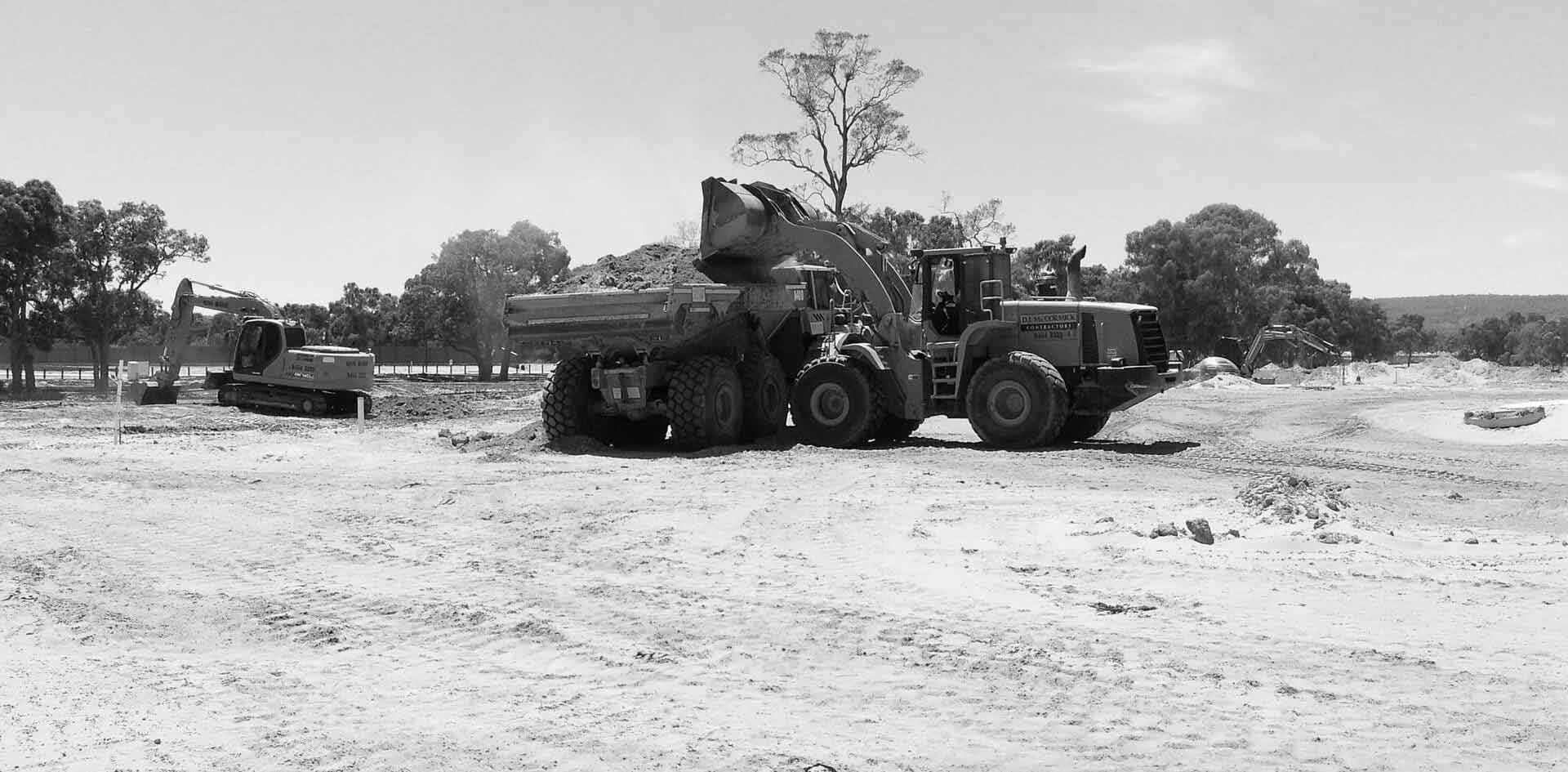 A frontloader wioth DJ MacCormick sign  filling a truck with sand. 